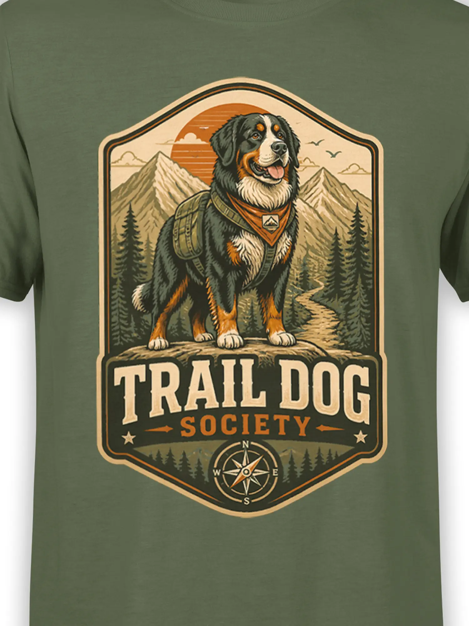 Close-up of trail dog society graphic showing hiking dog with pack, mountain backdrop, pine trees, and compass on olive green fabric