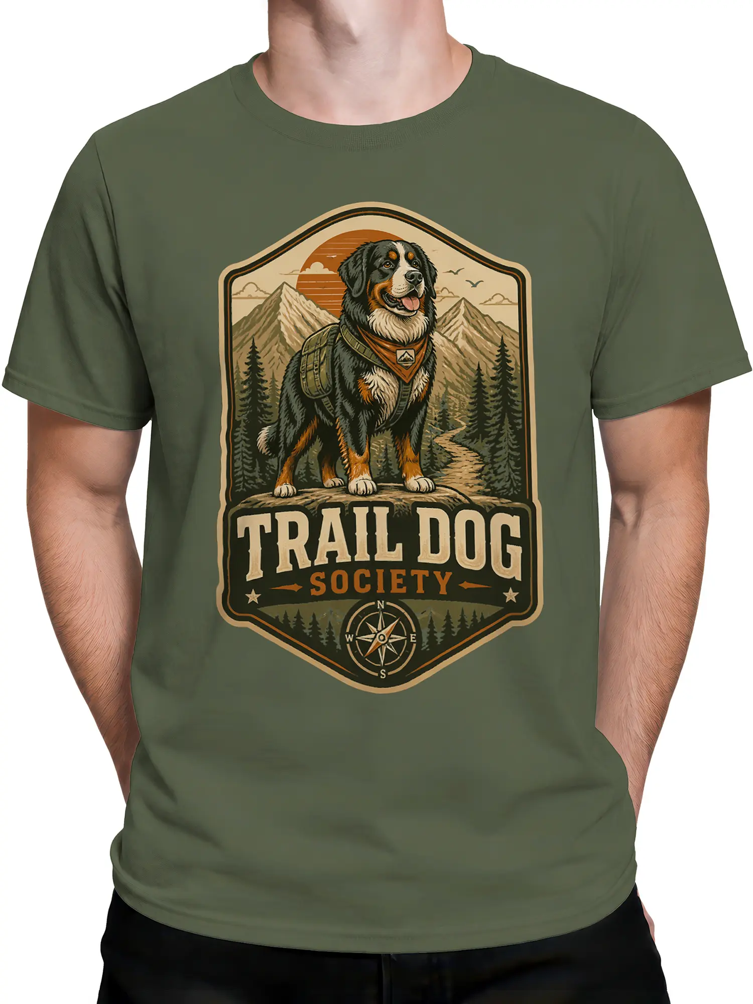 Man wearing olive green trail dog society shirt featuring hiking dog illustration and mountain landscape
