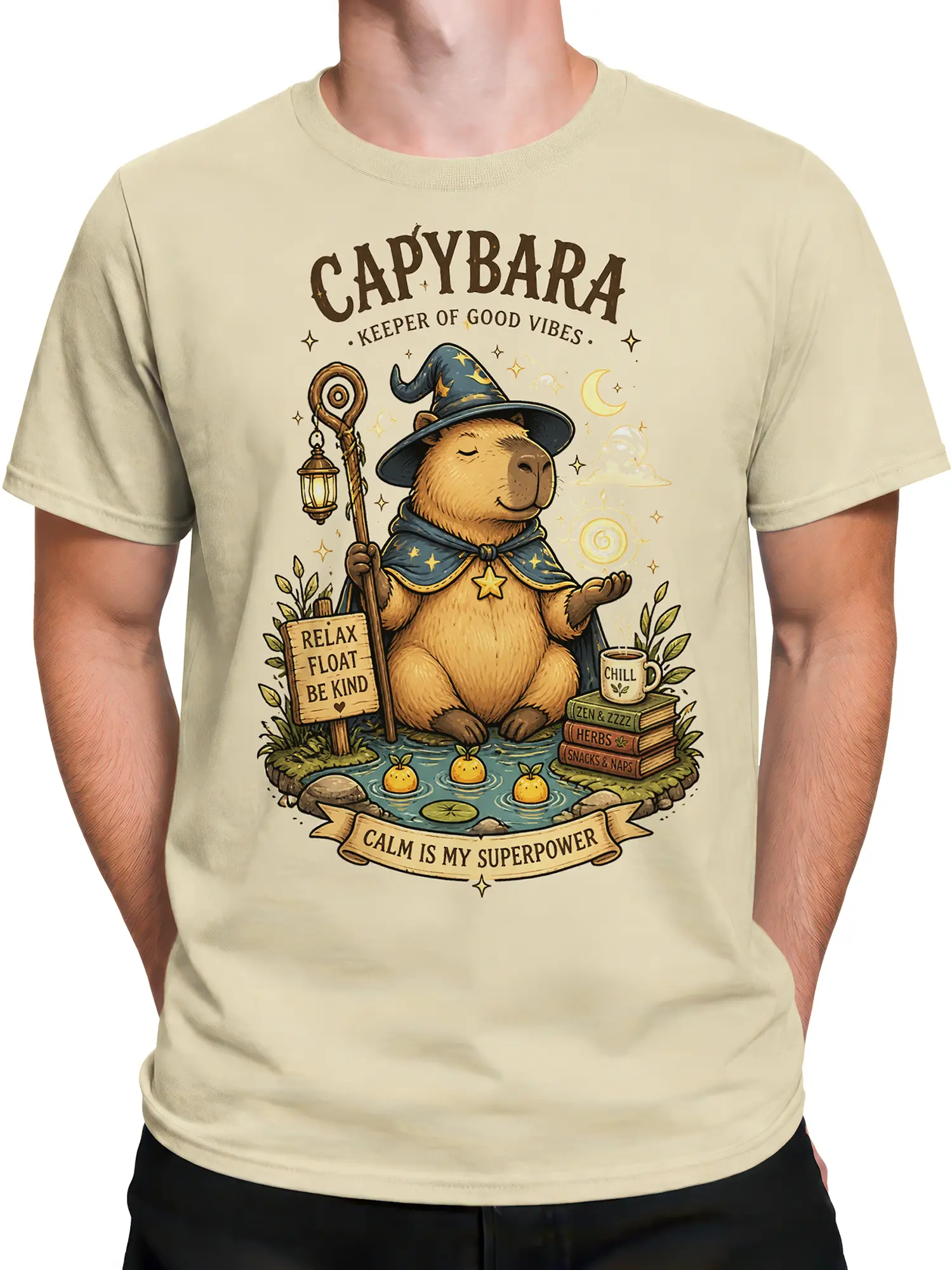 Male torso wearing a beige capybara wizard T-shirt with magical stars, pond details, and relaxing fantasy artwork