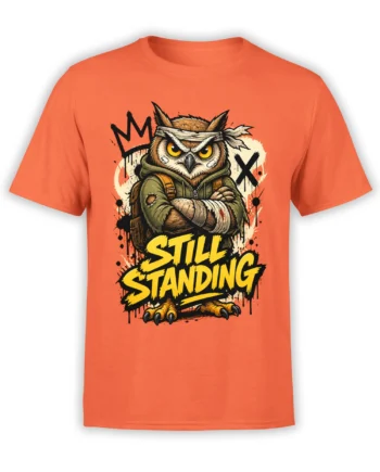 Battle-worn owl warrior with bandaged wings and “STILL STANDING” text on an orange T-shirt