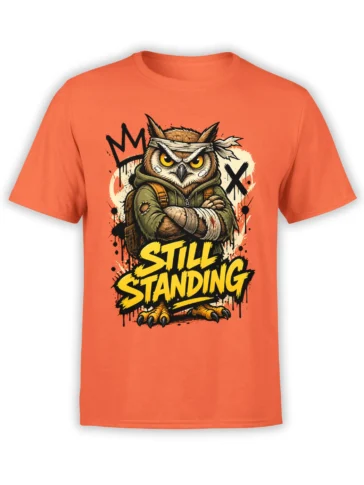 Battle-worn owl warrior with bandaged wings and “STILL STANDING” text on an orange T-shirt
