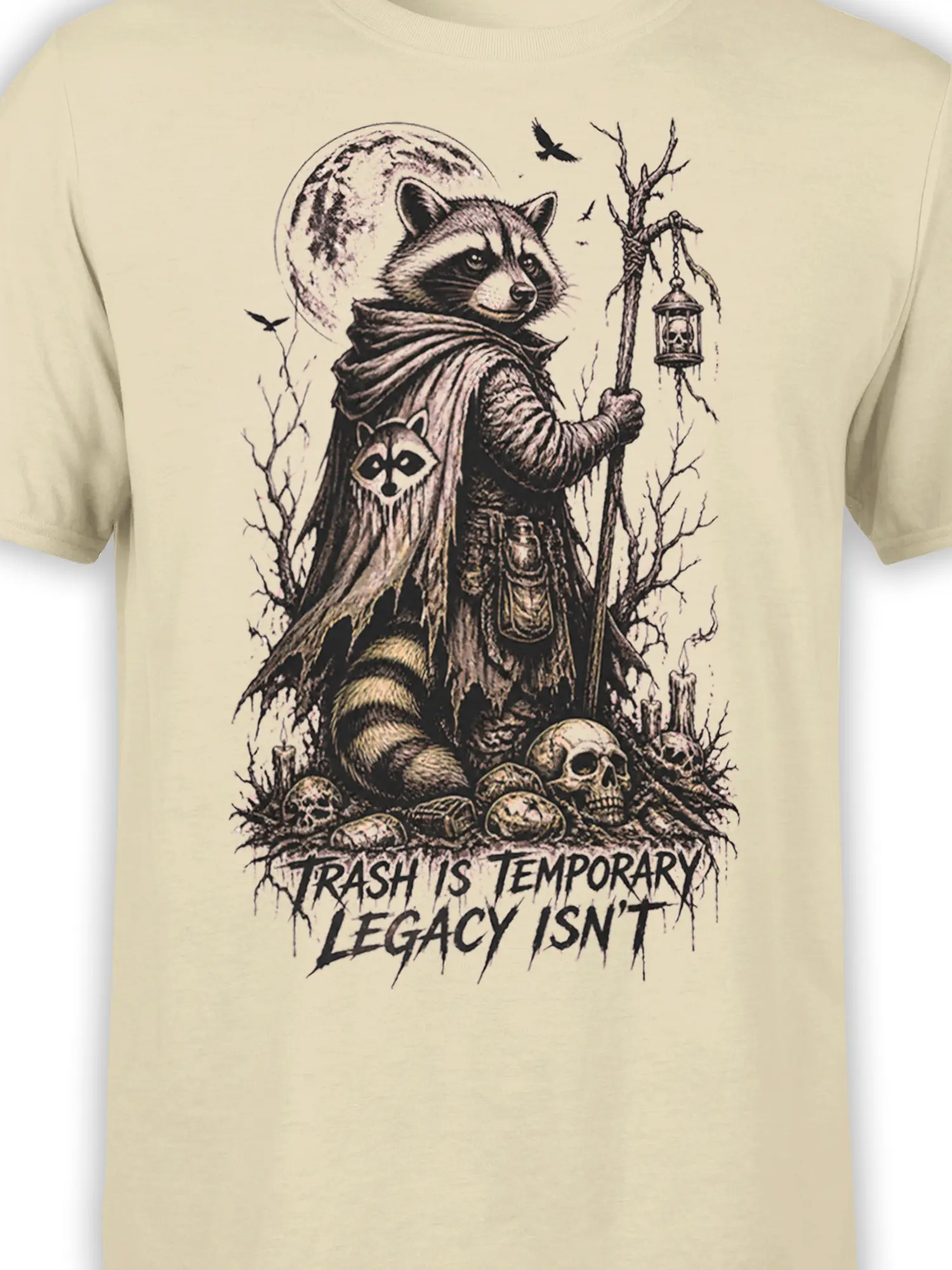 Close-up of the beige shirt graphic showing the raccoon, lantern, skulls, moon, ravens, and legacy slogan