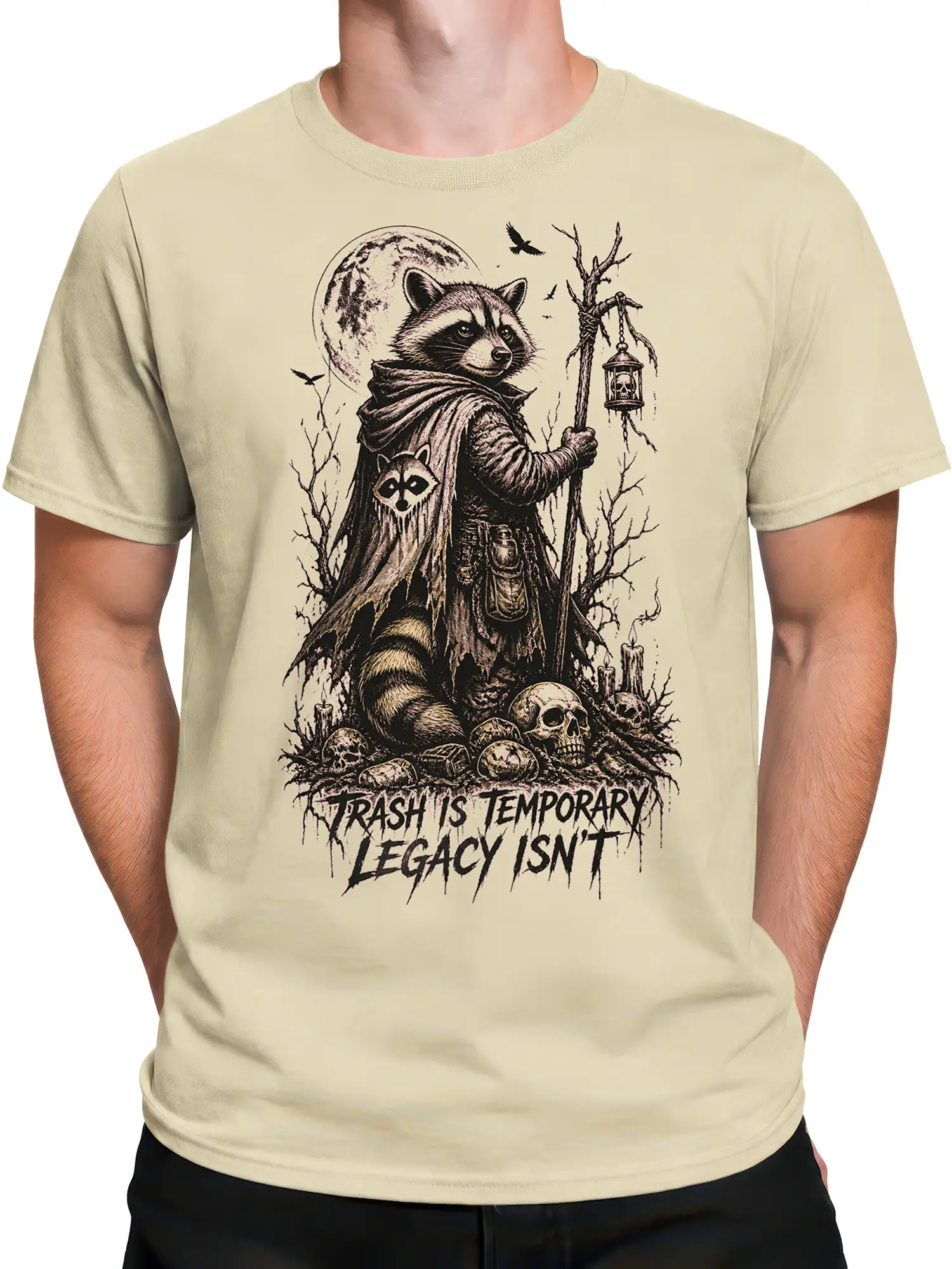Male torso wearing a beige T-shirt with a cloaked raccoon, lantern, skulls, and legacy slogan