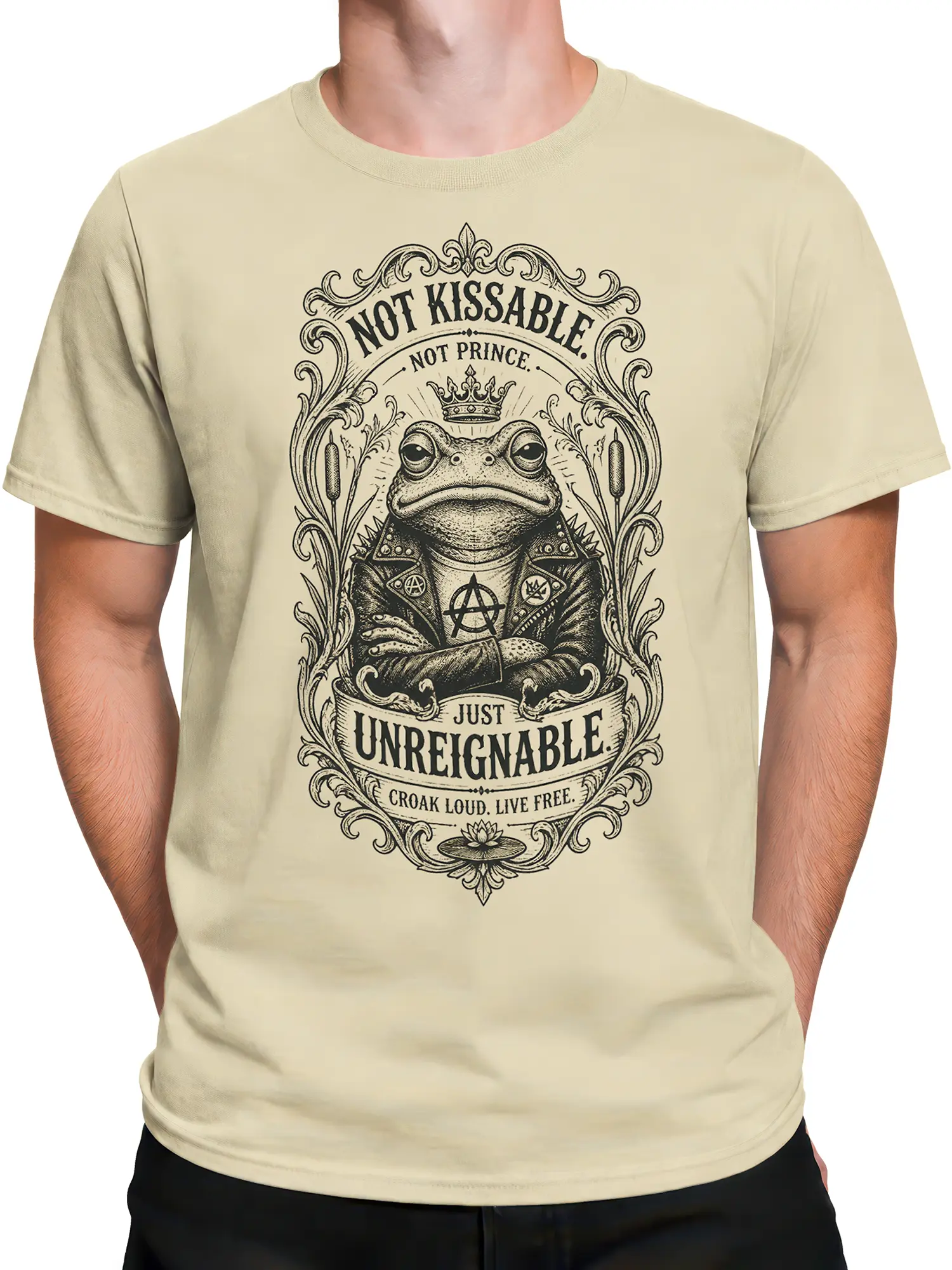 Male torso wearing a beige punk frog T-shirt with ornate artwork, crowned frog, and bold “Unreignable” design