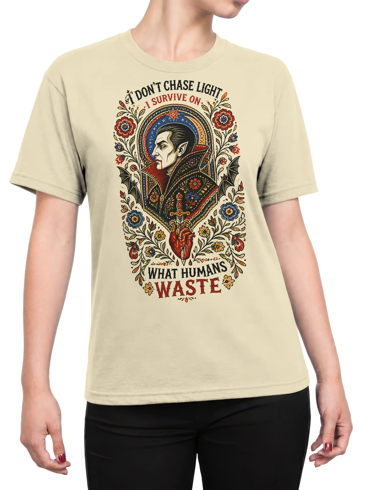 Female torso wearing a beige gothic vampire T-shirt with floral folk-art artwork, bats, a sword, heart, and lettering