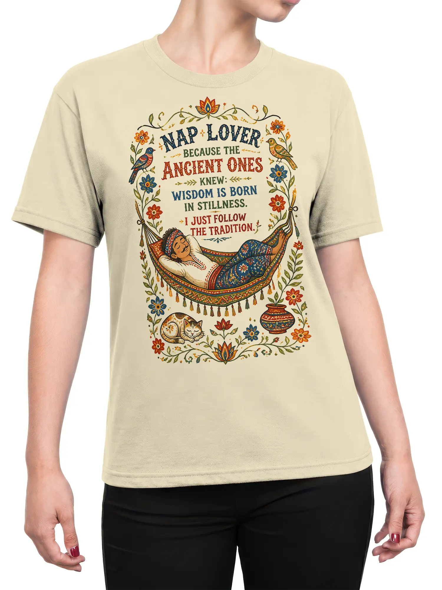 Female torso wearing a beige cat T-shirt with a colorful hammock nap scene, sleeping cat, flowers, birds, and wisdom lettering