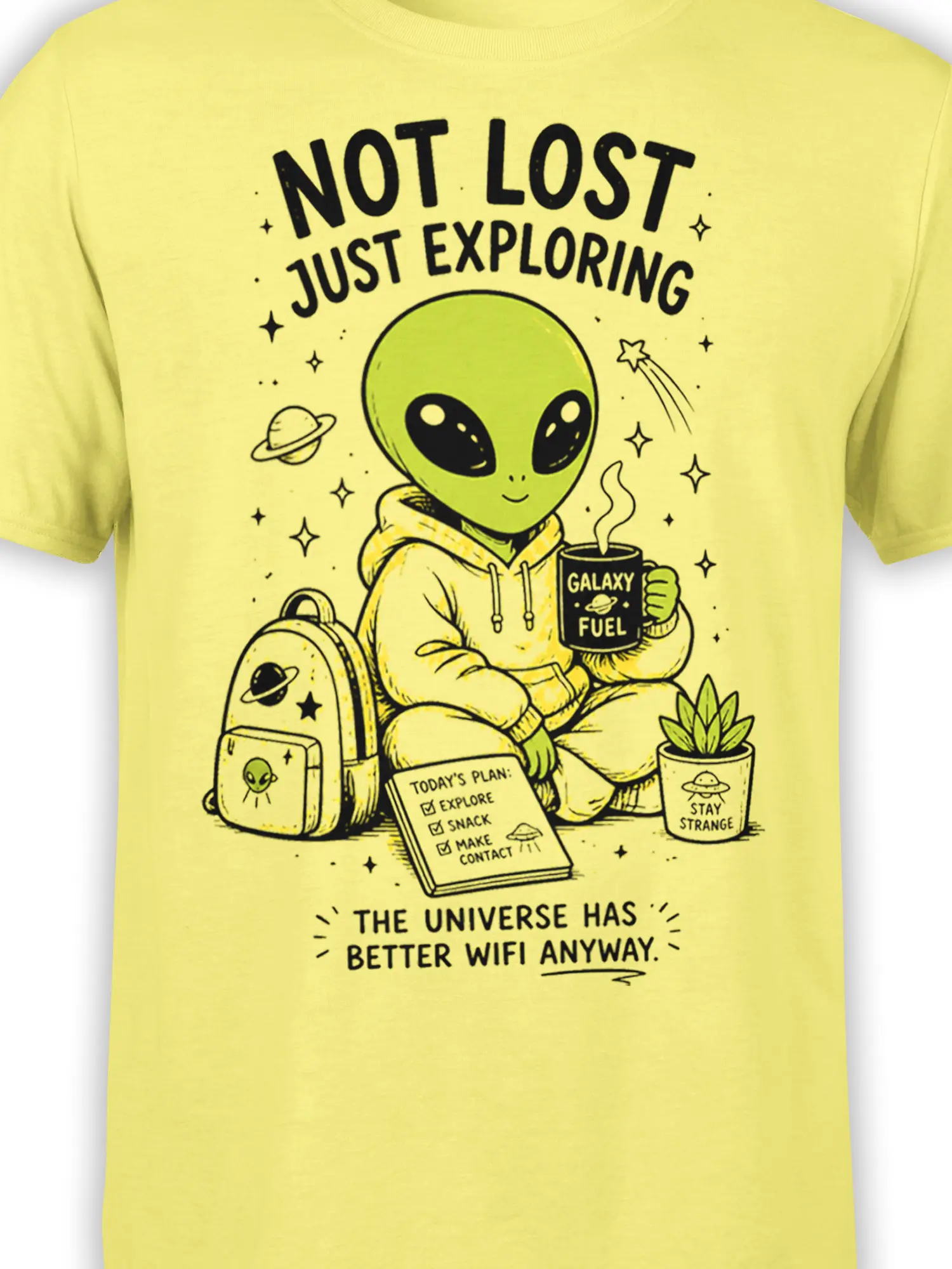 Close-up of green alien explorer artwork, galaxy fuel mug, backpack, stars, and space lettering on a yellow tee