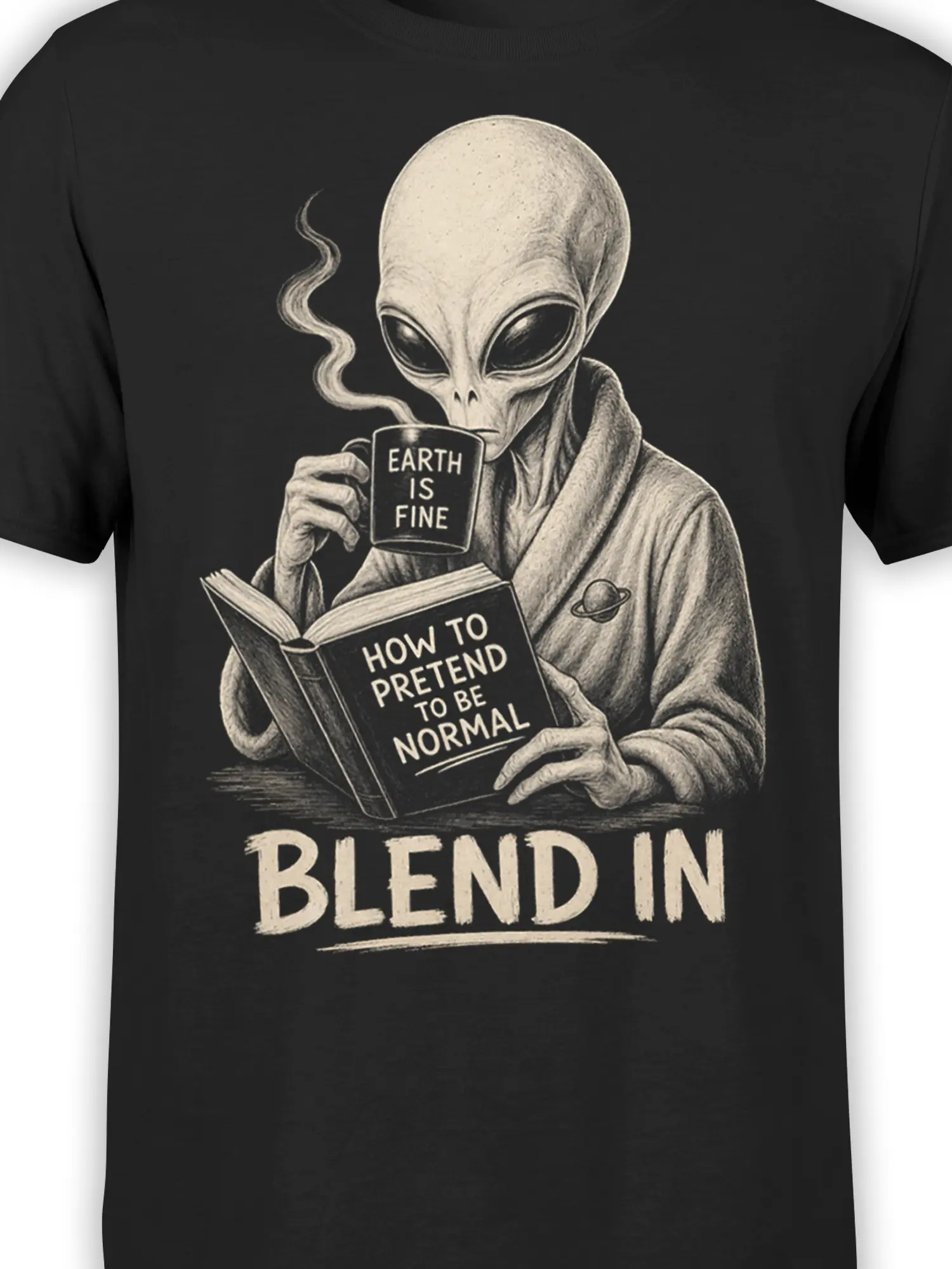 Close-up of the alien, coffee mug, book text, and cream “BLEND IN” design on a black shirt