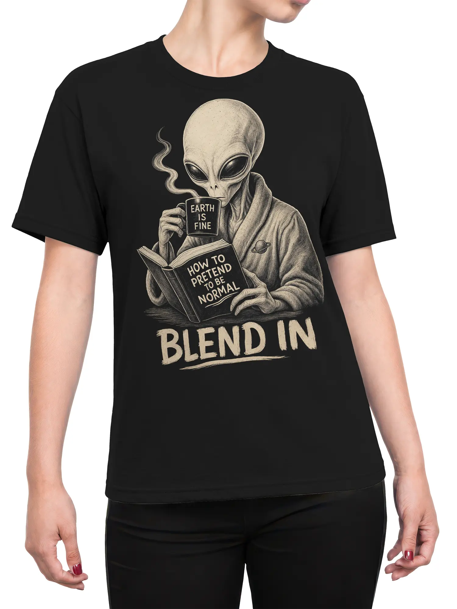Female torso wearing a black alien graphic tee with coffee mug, book, and “BLEND IN” artwork