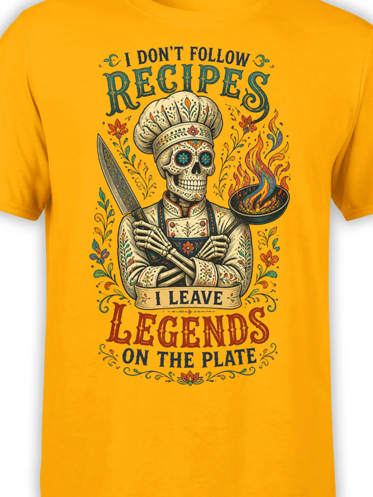 Close-up of skeleton chef artwork, flaming pan, knife, flowers, and vintage lettering on a yellow T-shirt