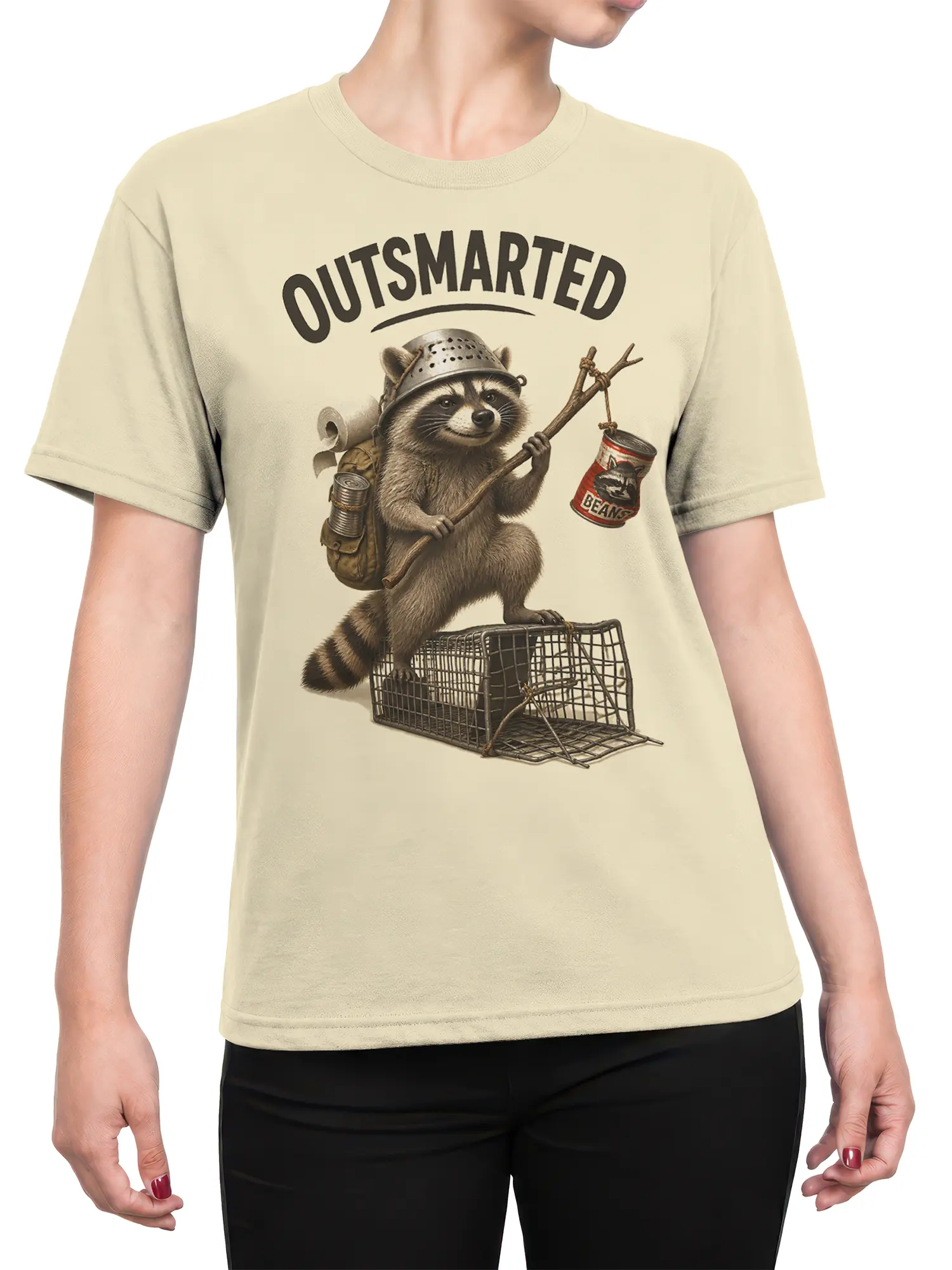 Female torso wearing a beige raccoon T-shirt with an “OUTSMARTED” escape illustration and bean can detail