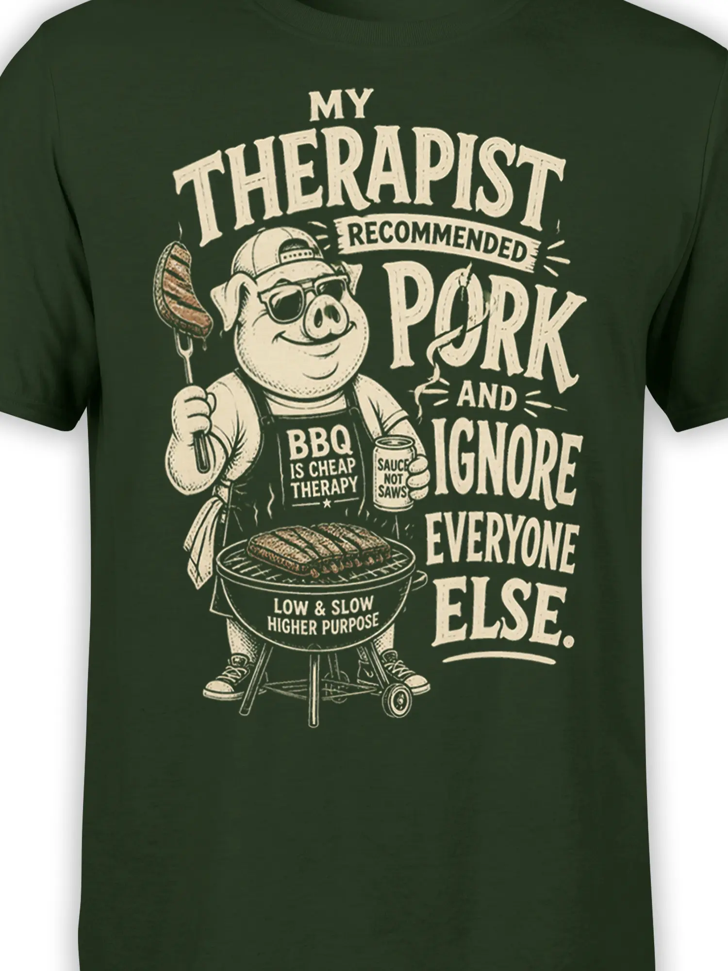 Close-up of cream pig barbecue artwork, sunglasses, grill, sauce, and bold humorous lettering on a green shirt