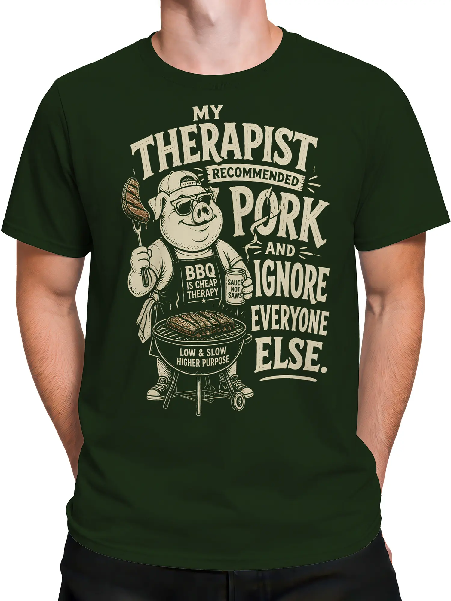 Male torso wearing a green pig barbecue T-shirt with grill artwork, sauce details, and retro cream lettering