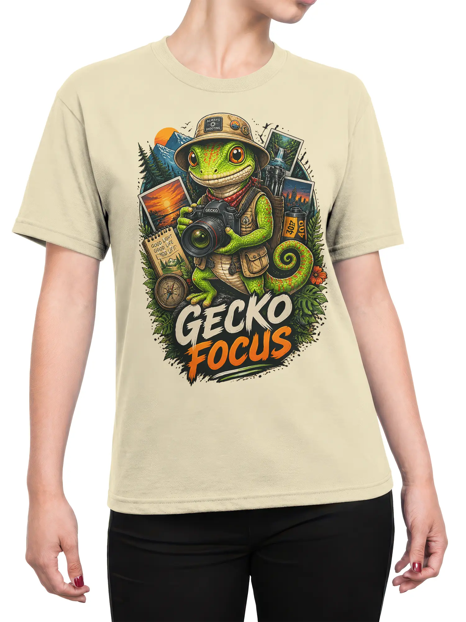 Female torso wearing a beige gecko photographer T-shirt with camera artwork, mountain scenes, and GECKO FOCUS lettering