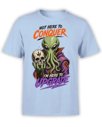 Green alien holding a cracked skull on a light blue shirt with bold “Not Here to Conquer” lettering