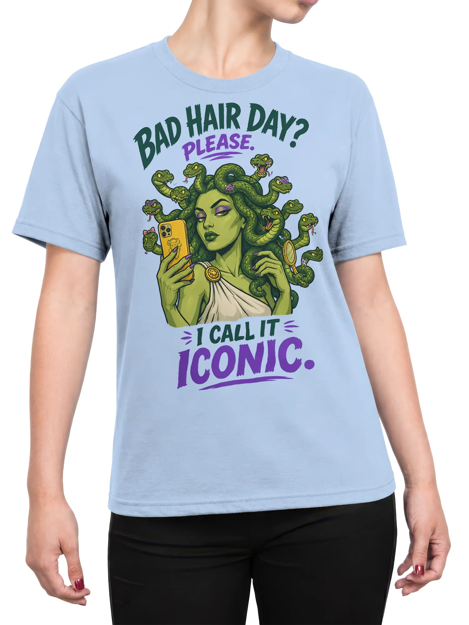 Female torso wearing a light blue Medusa graphic tee with snake hair, phone, mirror, and playful fantasy lettering