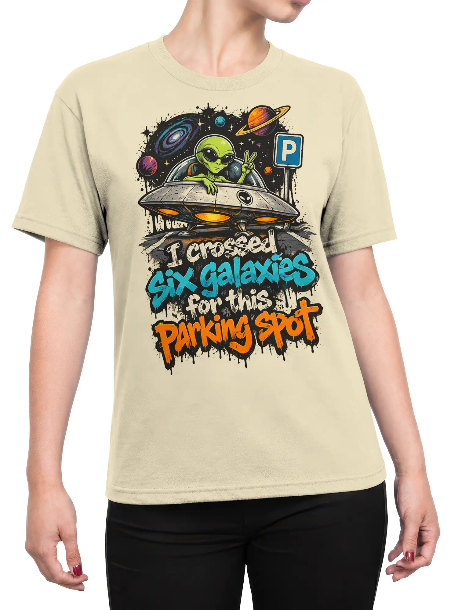 Female torso wearing a beige alien graphic tee with a flying saucer, galaxy scene, and colorful parking message