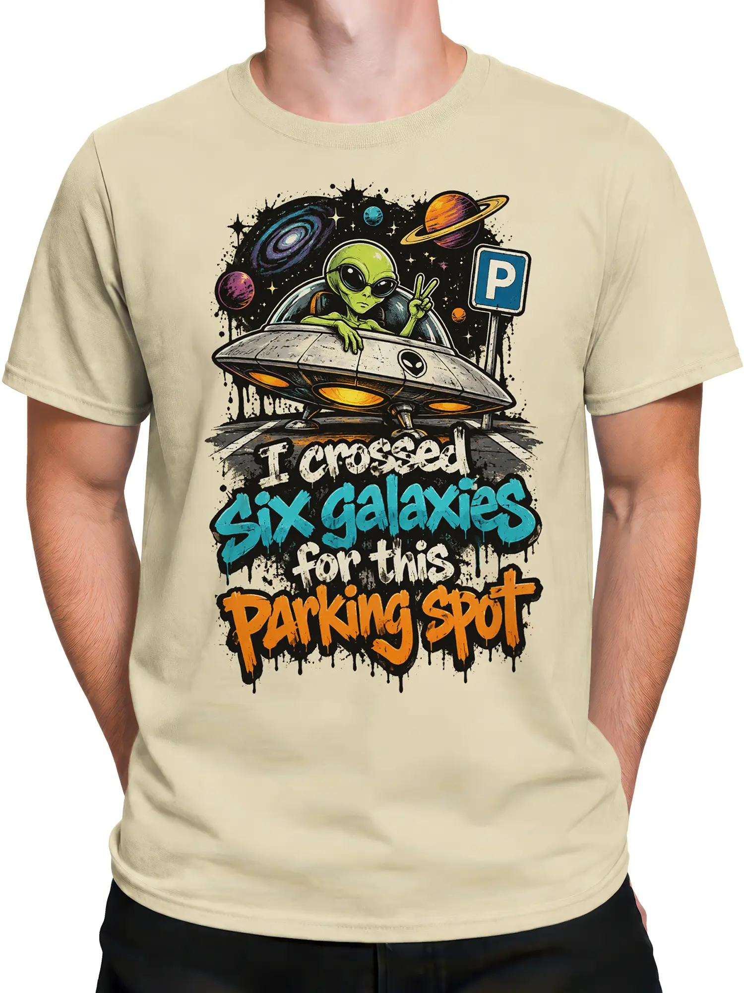 Male torso wearing a beige alien graphic tee with a flying saucer, planets, and bold cosmic parking text