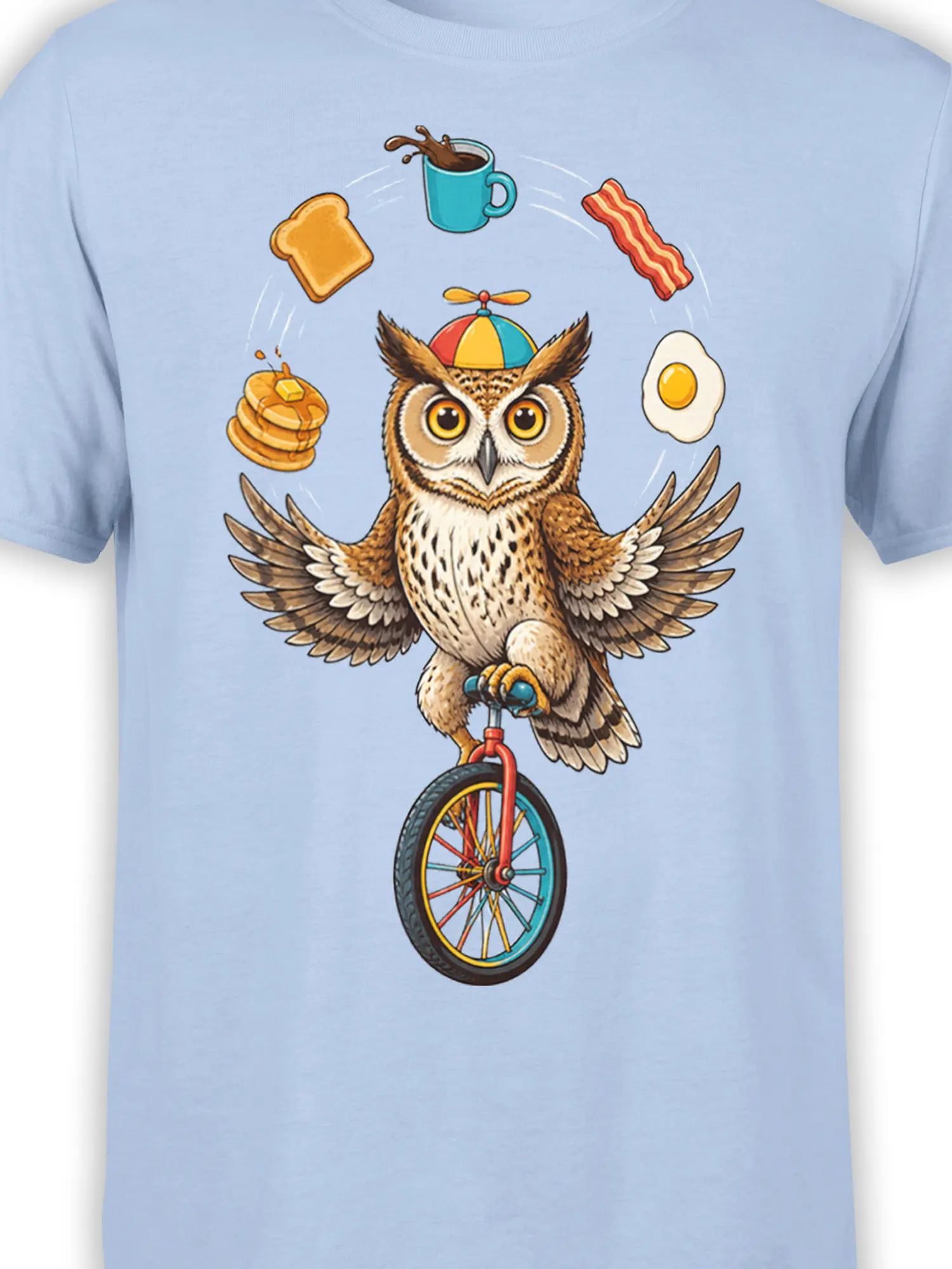 Close-up of the colorful balancing owl, unicycle, and breakfast food design on a light blue shirt