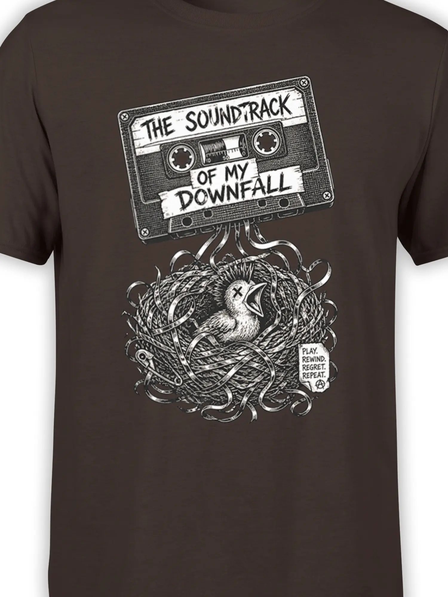 Close-up of the brown tee design showing the cassette tape, chick, tangled nest, and “Play Rewind Regret Repeat” text