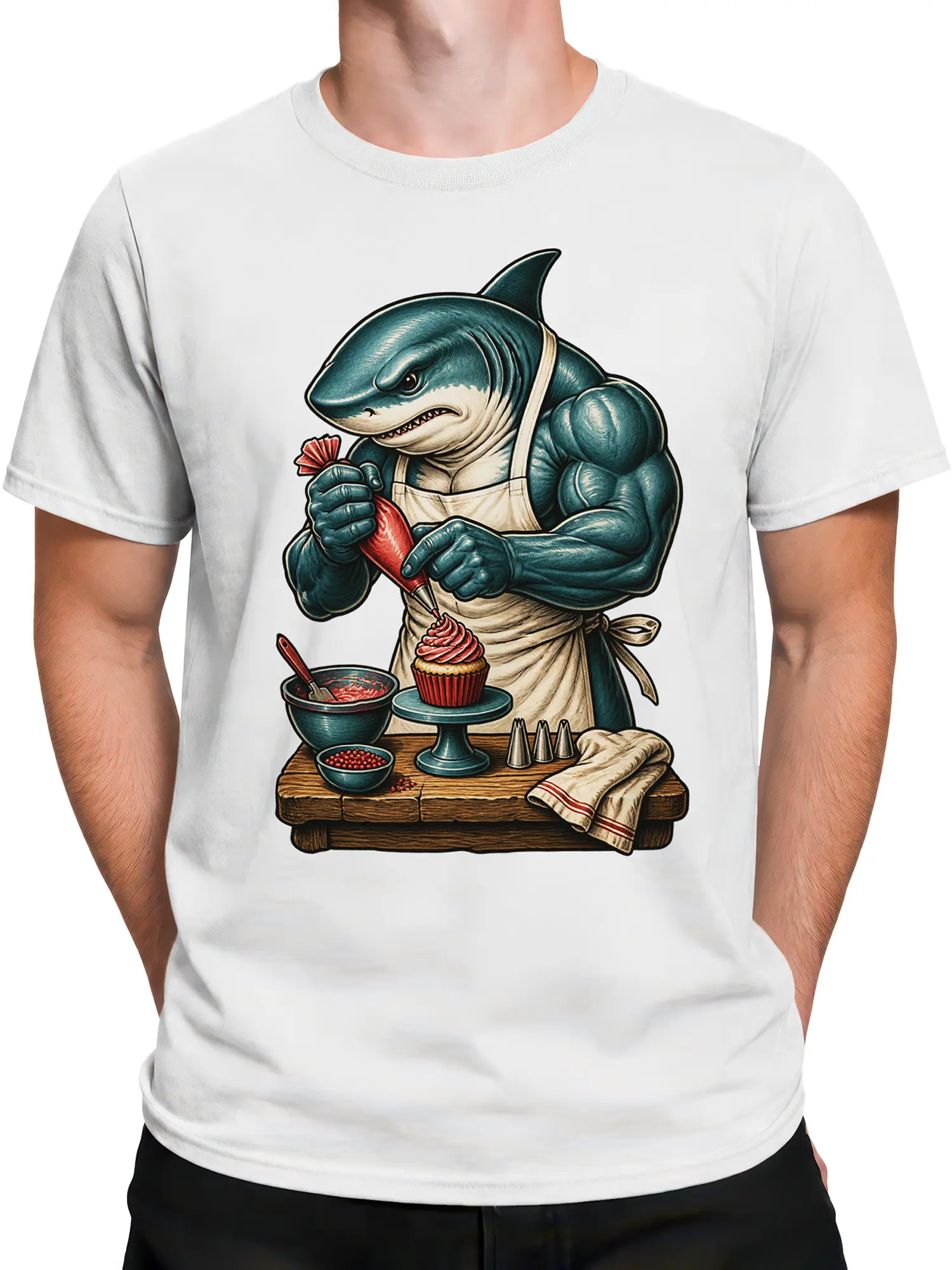 Male torso wearing a white T-shirt with a blue shark baker decorating a cupcake