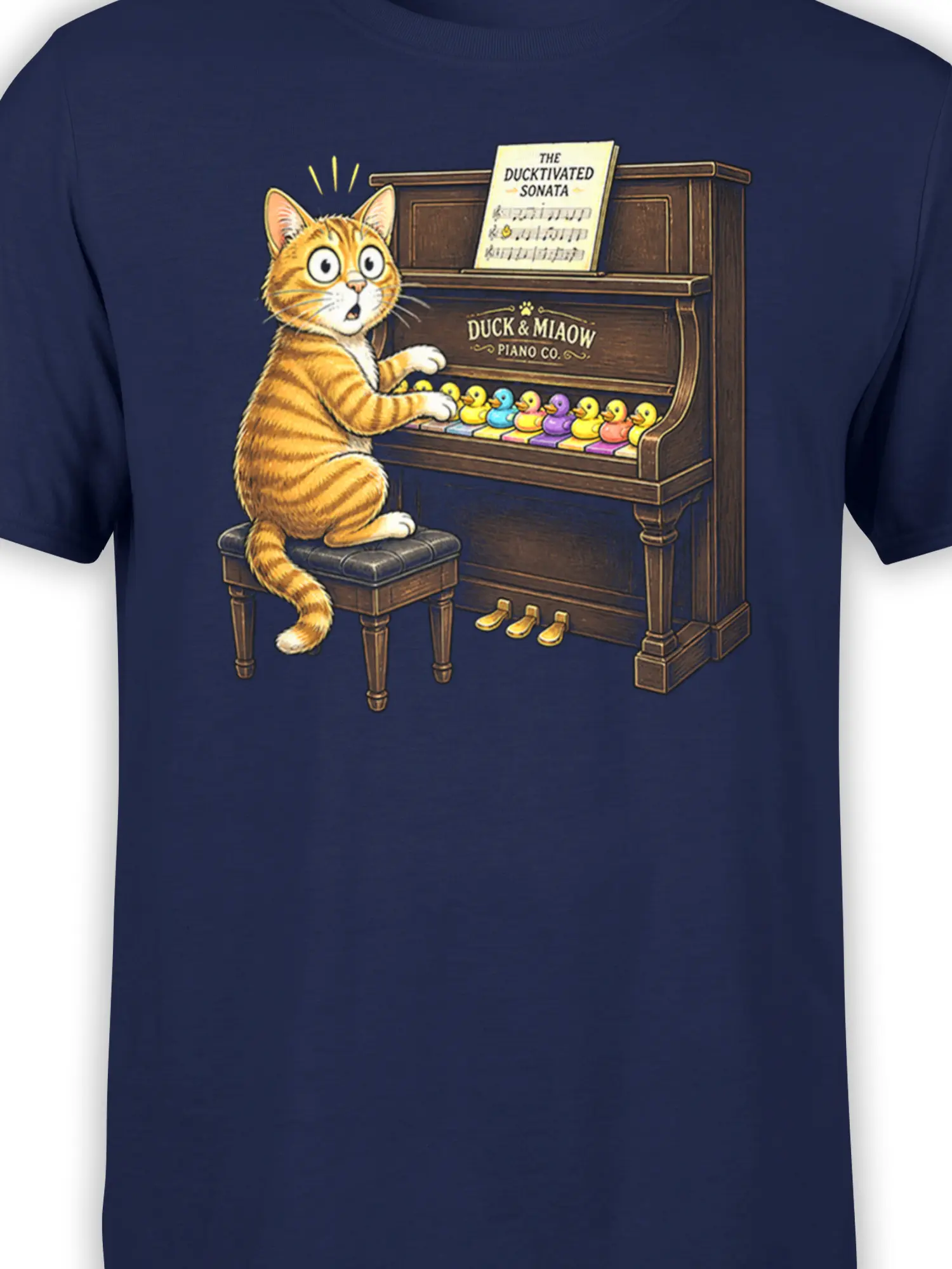 Close-up of orange tabby cat, piano keys, colorful ducks, and music sheet on navy T-shirt