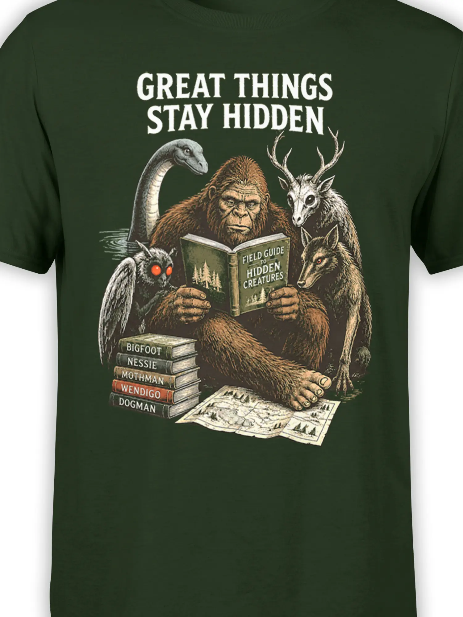 Close-up of hidden creatures, glowing eyes, books, and field-guide details on a green cryptid T-shirt