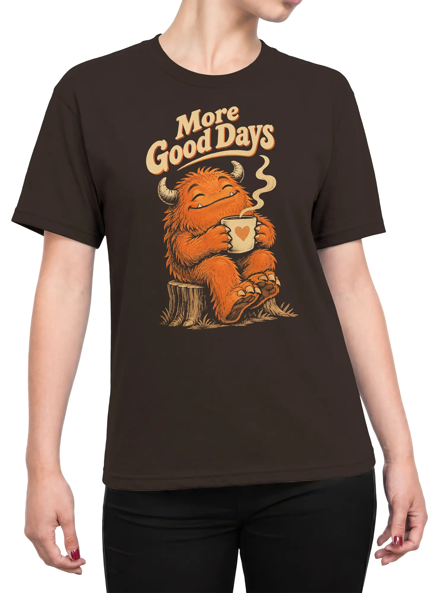 Female torso wearing a dark brown T-shirt with a smiling orange monster and “More Good Days” coffee design