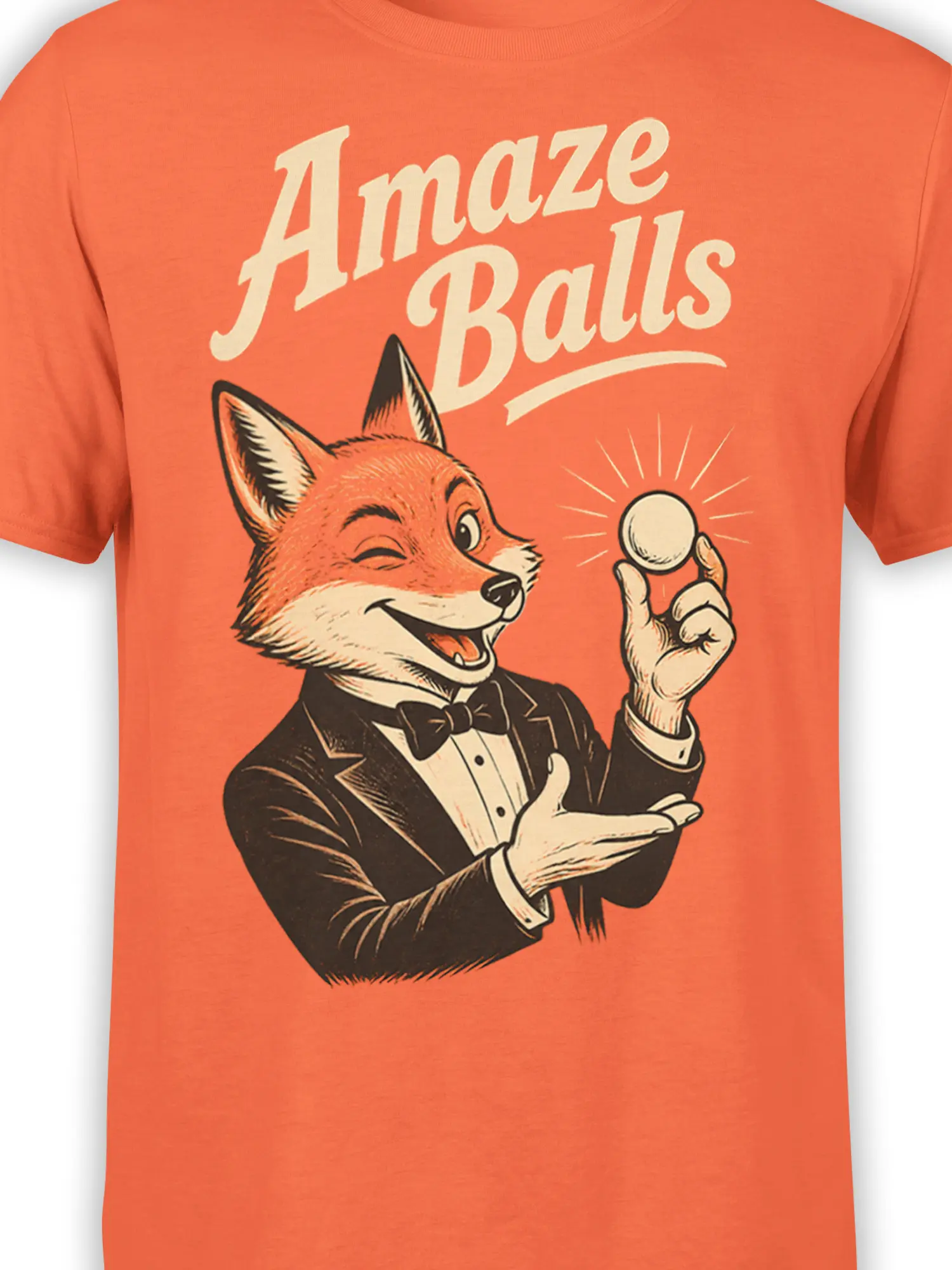 Close-up of the tuxedo fox magician, round ball, and vintage “Amaze Balls” design on an orange shirt
